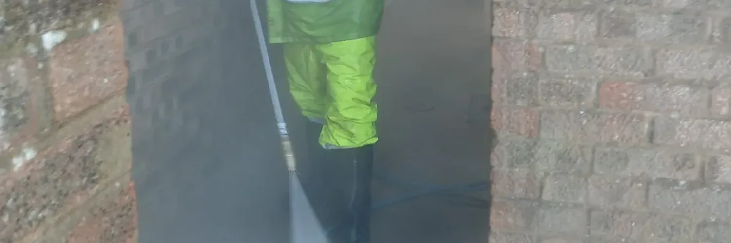 Worker in hi-vis PPE pressure washing brick undercroft passageway at residential apartment block, Northampton March 2026