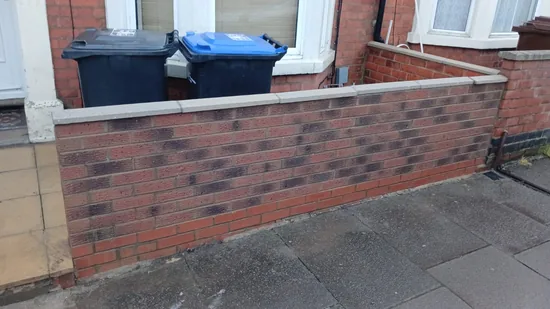Before - residential red brick garden wall with black staining across the top course, Northampton.