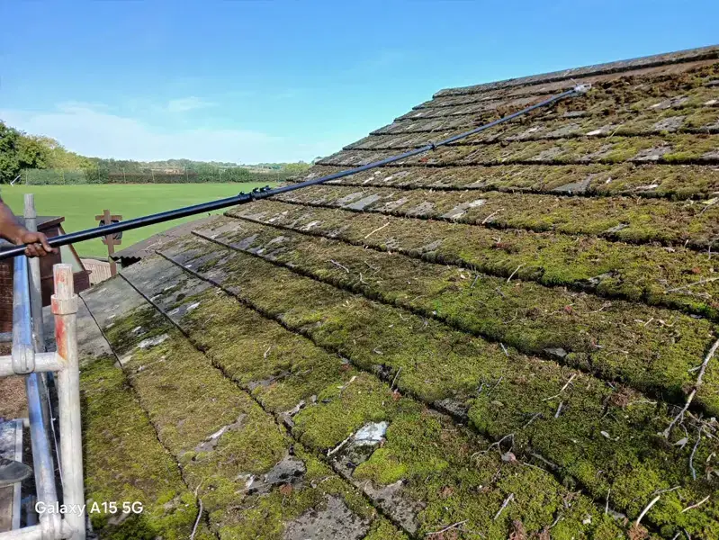 ECS operative hand-scraping moss off a tiled roof from a scaffold tower