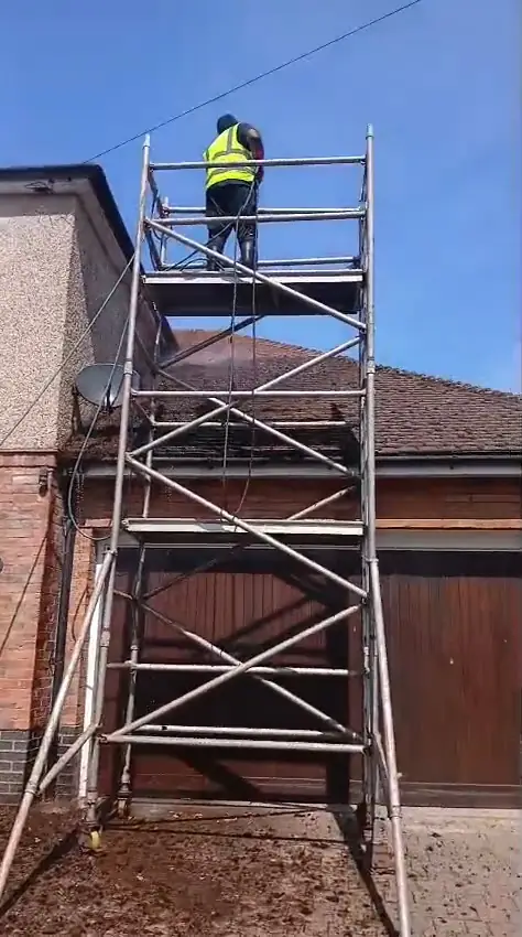ECS operative scraping a tiled roof from a scaffold tower on a two-storey home